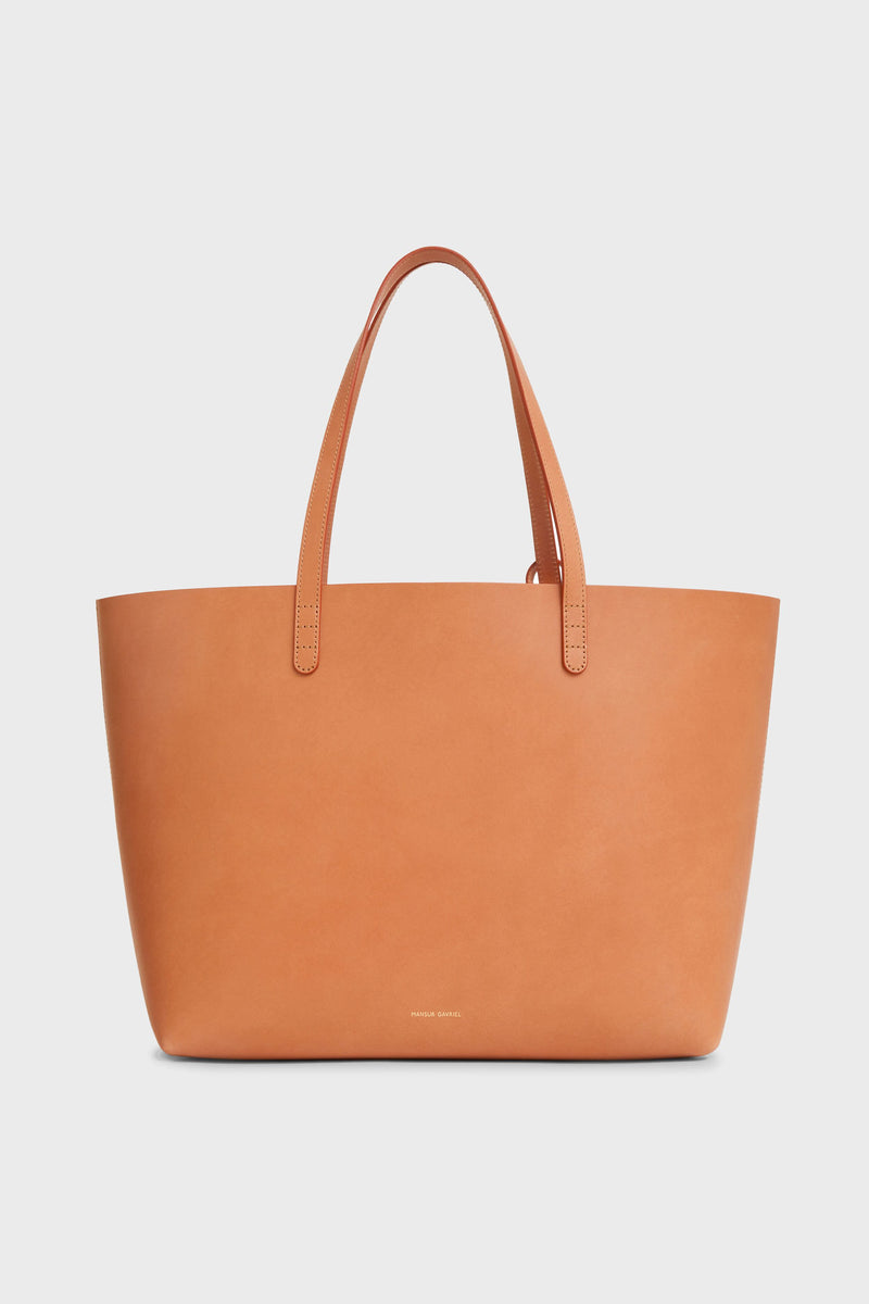 The Mansur Gavriel tan Italian leather tote features two handles, a minimalist design, a small logo near the bottom, and a spacious interior—combining functionality with timeless elegance for work.