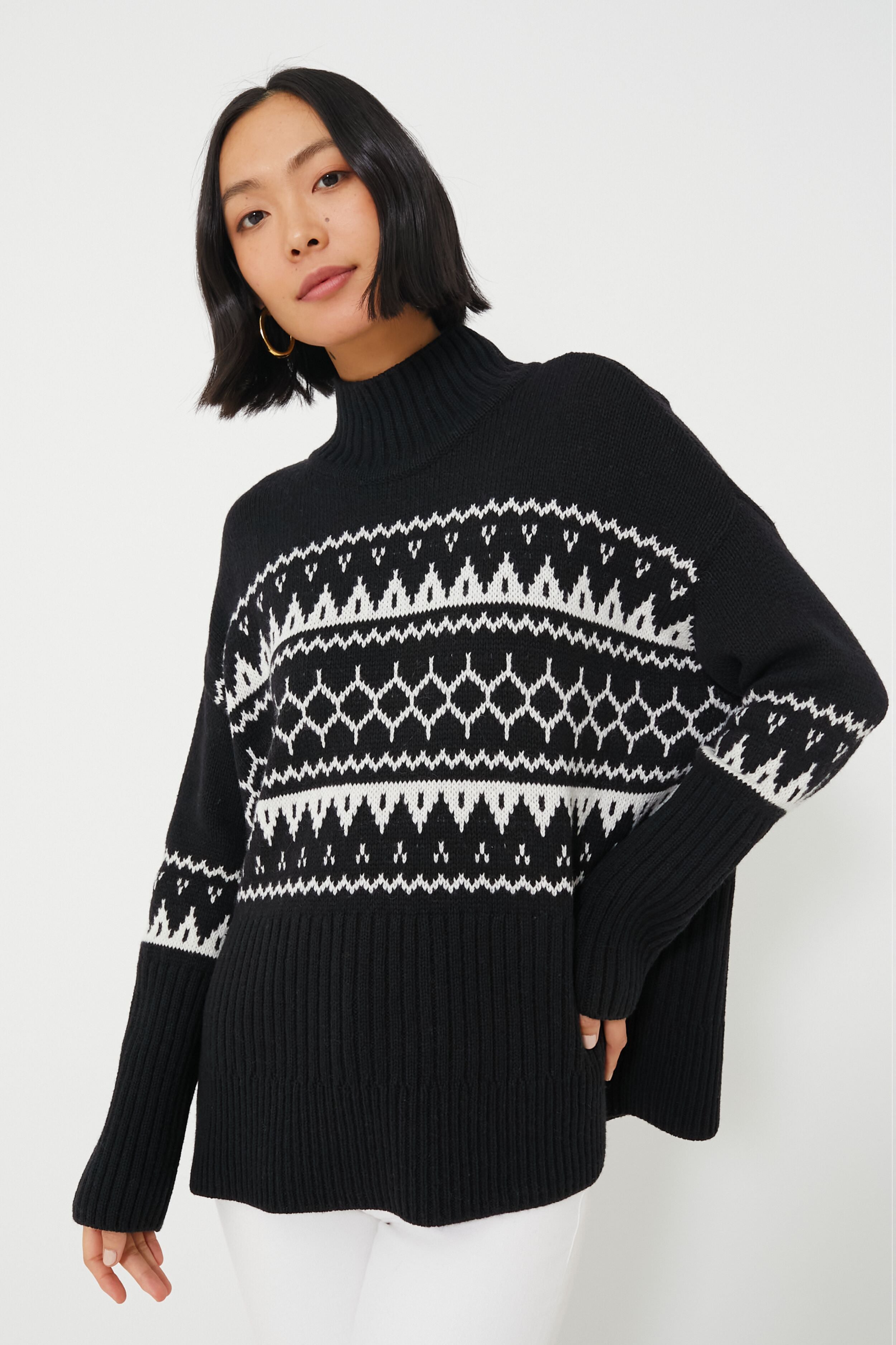 A woman in a Barbour black turtleneck sweater with white geometric patterns, paired with white pants.
