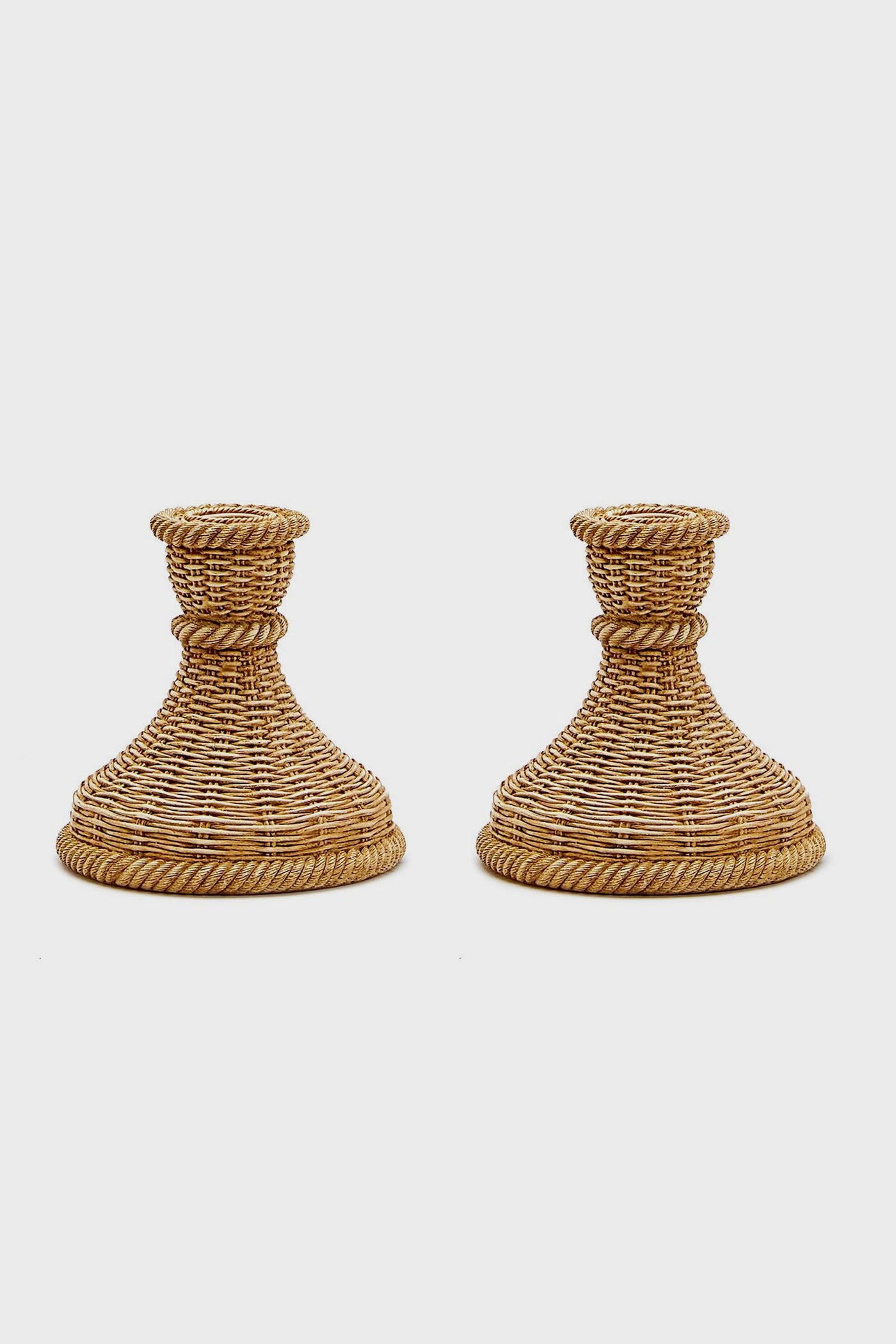 A pair of woven rattan candle holders by Two's Company, featuring wide bases and flared tops—ideal for bringing coastal charm to your home decor.