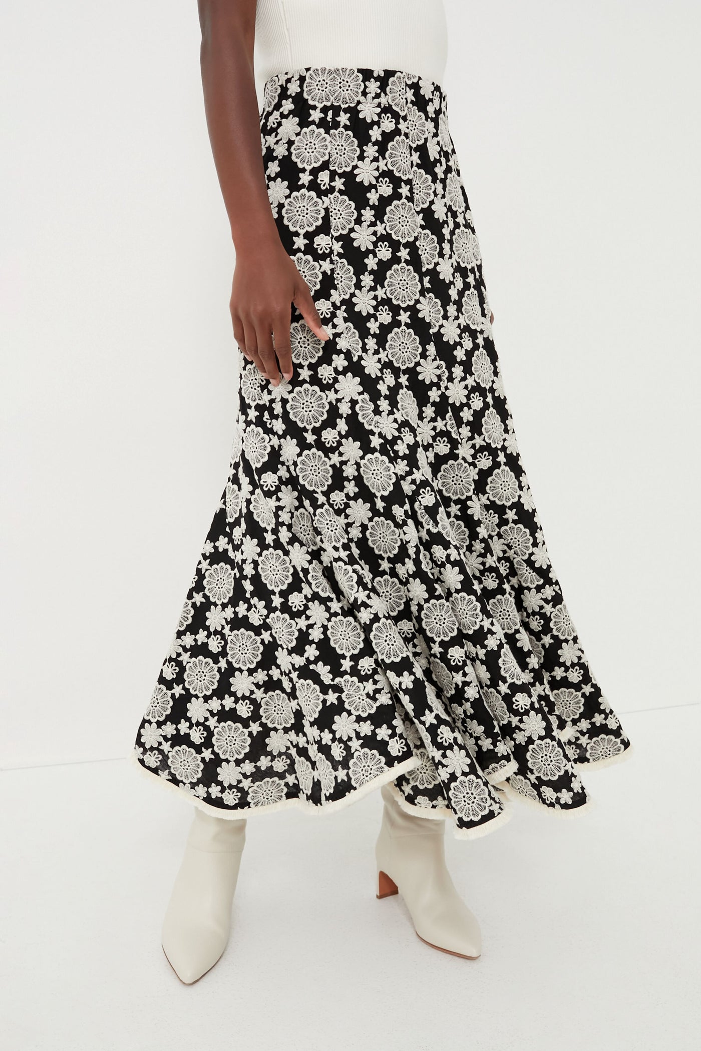 Someone is dressed in a Hyacinth House black A-line maxi skirt with white floral patterns, paired with a white top and white heeled boots.