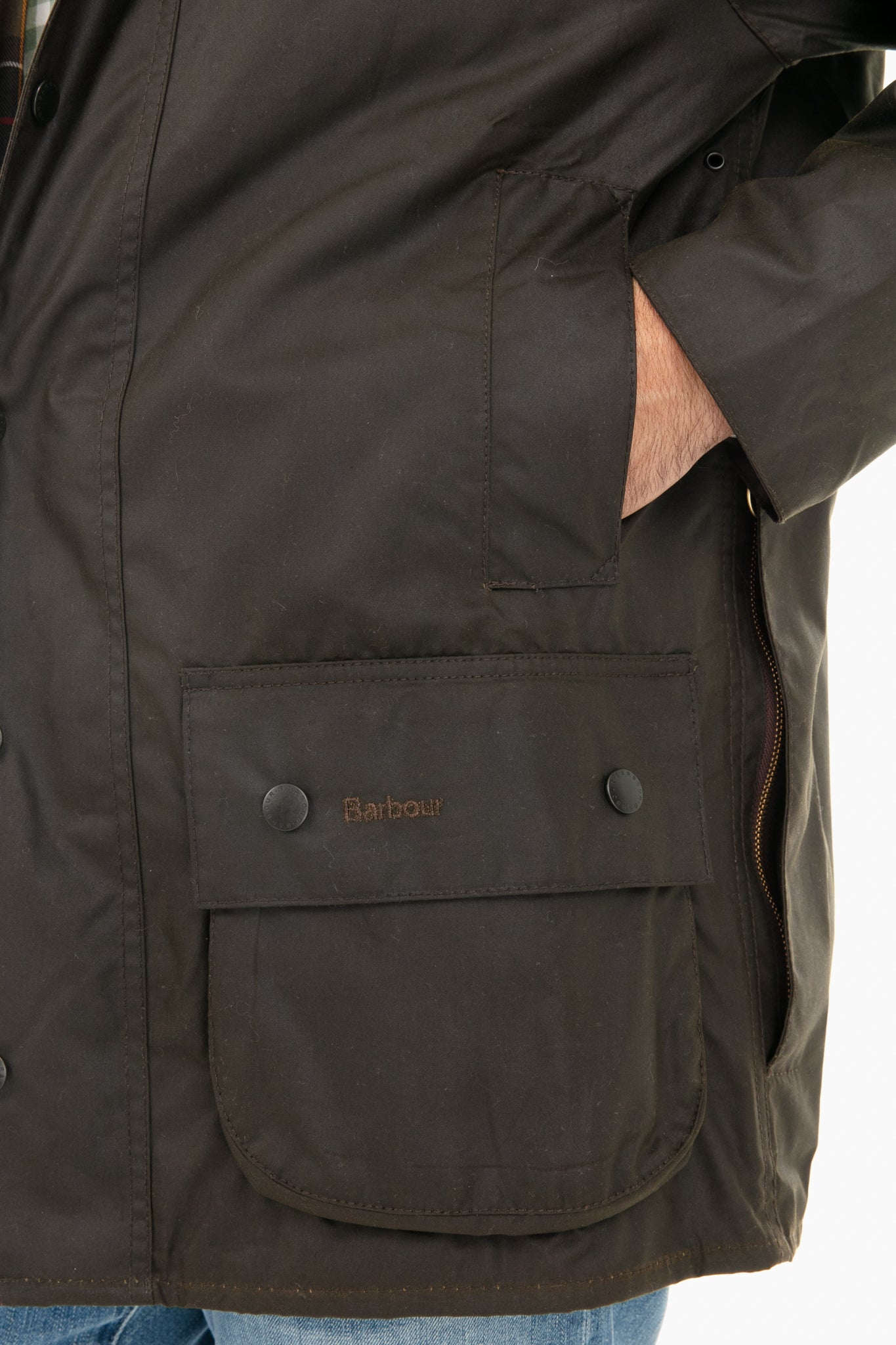 A person wears a dark Barbour Classic Beaufort jacket, hand in the side pocket. The Barbour logo appears on the front pocket flap of this iconic waxed cotton jacket.