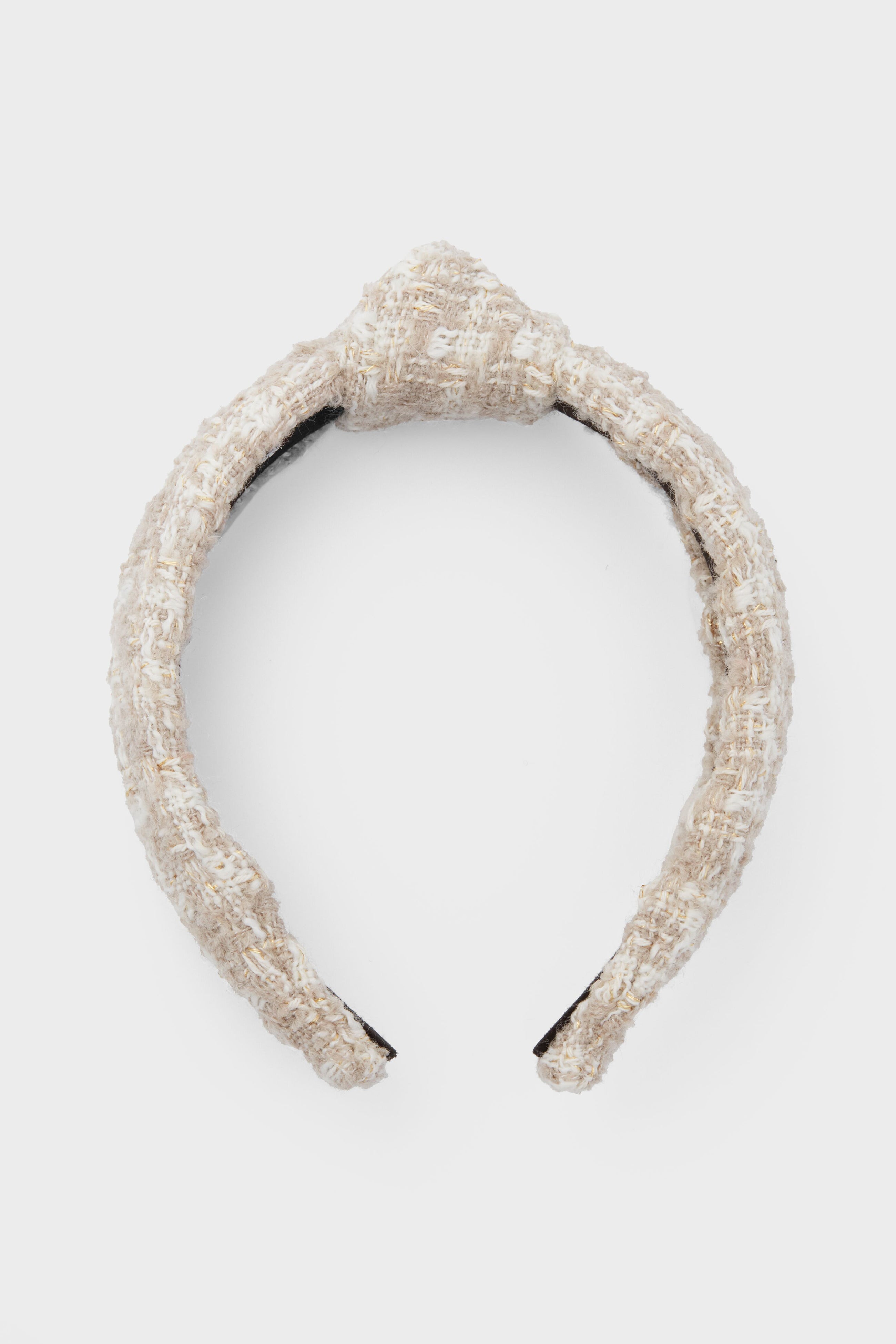 A beige tweed headband by Lele Sadoughi features a textured design with a central knot, inspired by the brand's signature style.