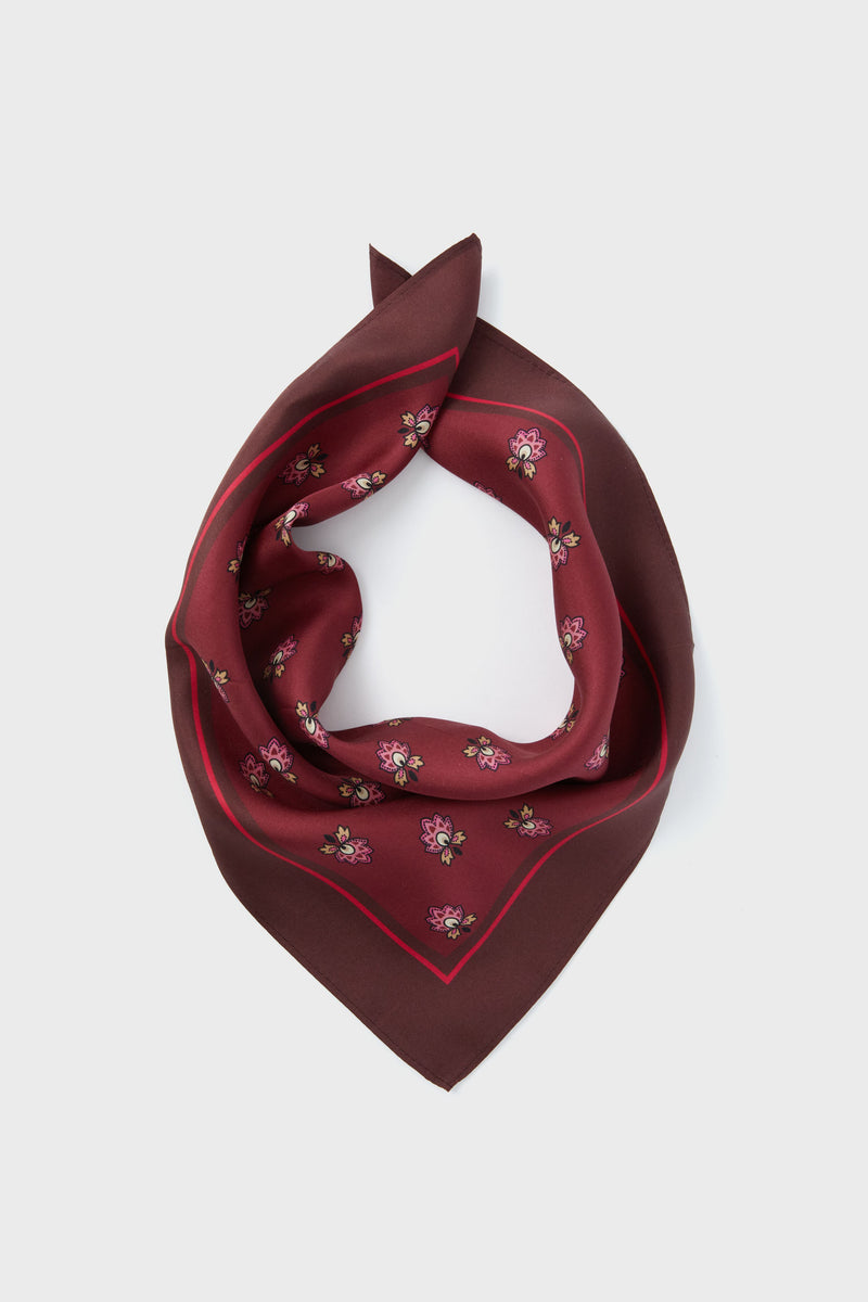 A maroon silk scarf by Tuckernuck Accessories, featuring a small mulberry floral print and folded in a triangular shape, crafted from 100% silk.