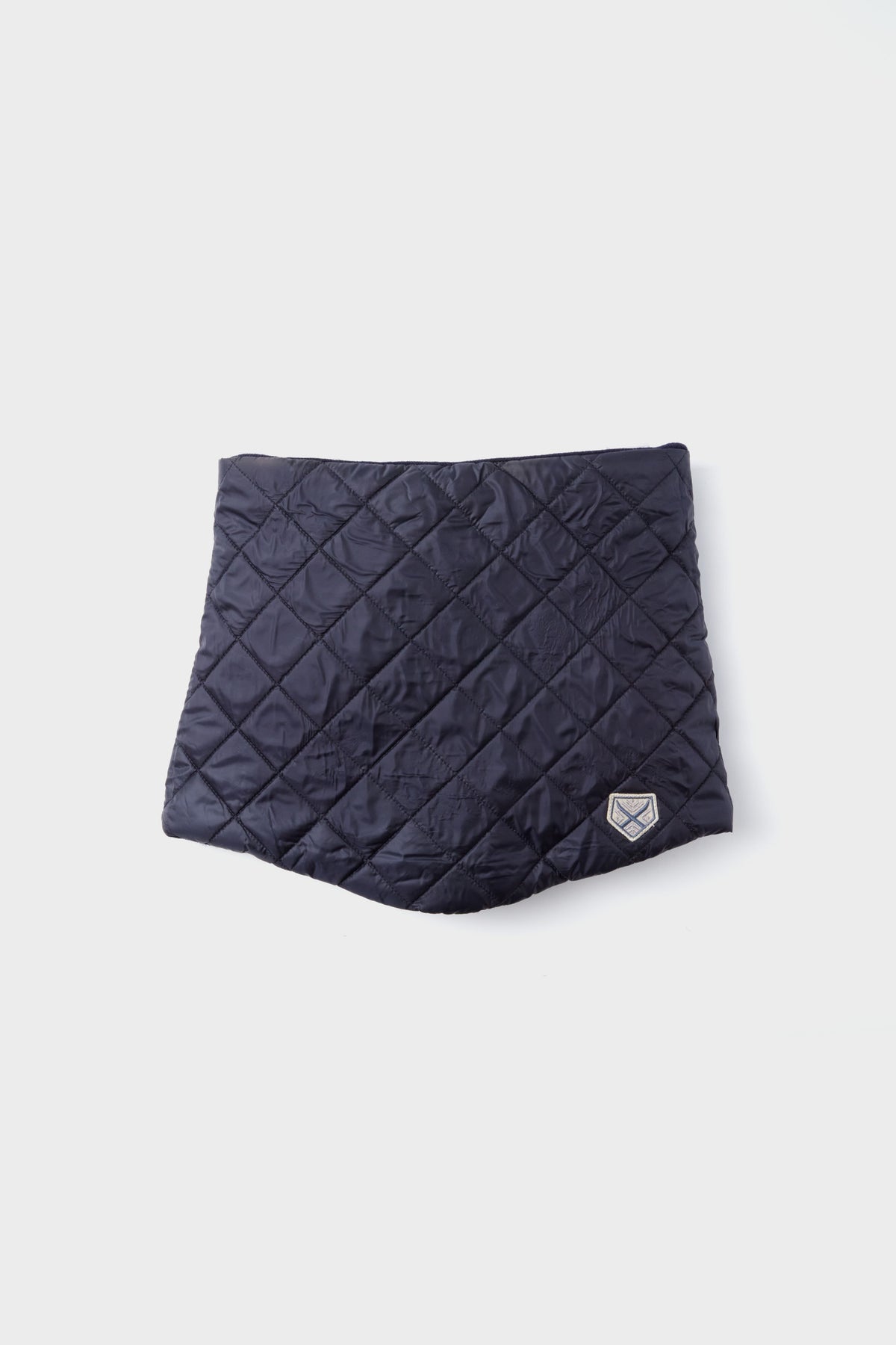 Quilted dark blue cover with diamond pattern and a small logo patch on the lower right, crafted from recycled nylon—an elegant winter accessory from the Powder Puff Collection.