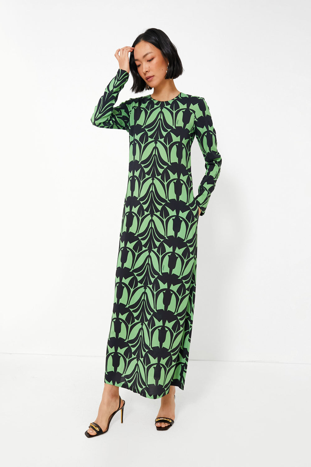 A woman wears a long-sleeve, floor-length La DoubleJ Papyrus Dress with a green and black leaf pattern, embodying Italian fashion elegance.