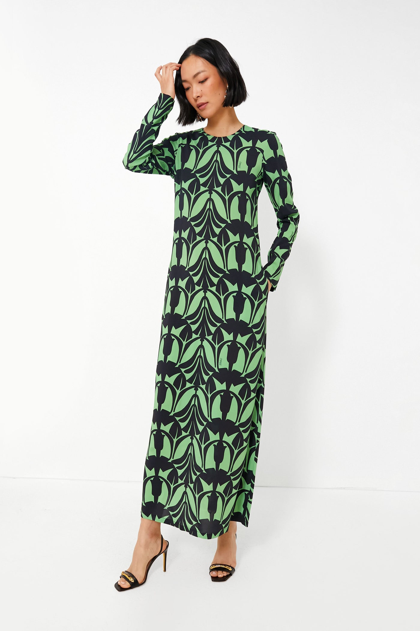 A woman wears a long-sleeve, floor-length La DoubleJ Papyrus Dress with a green and black leaf pattern, embodying Italian fashion elegance.