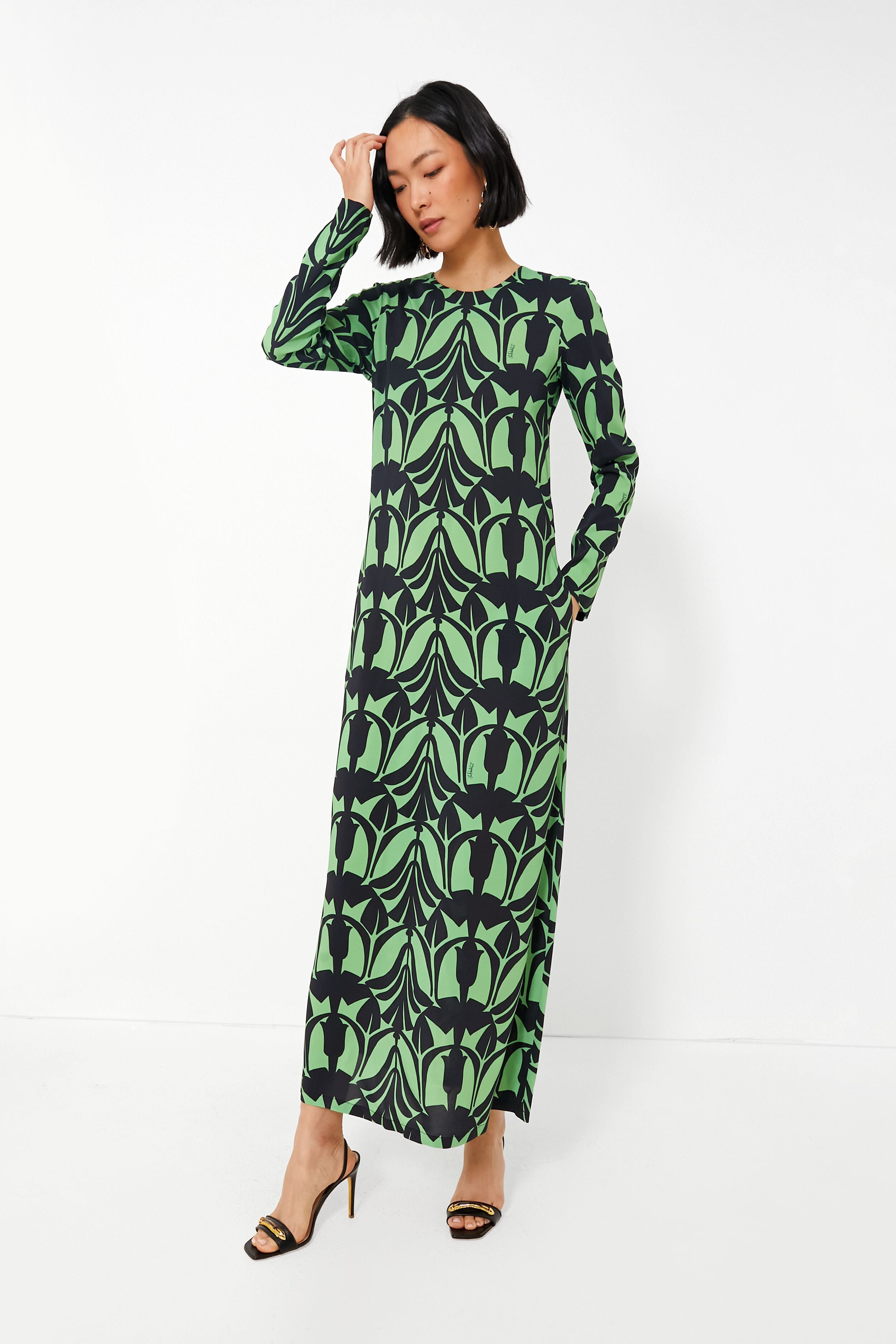A woman wears a long-sleeve, floor-length La DoubleJ Papyrus Dress with a green and black leaf pattern, embodying Italian fashion elegance.