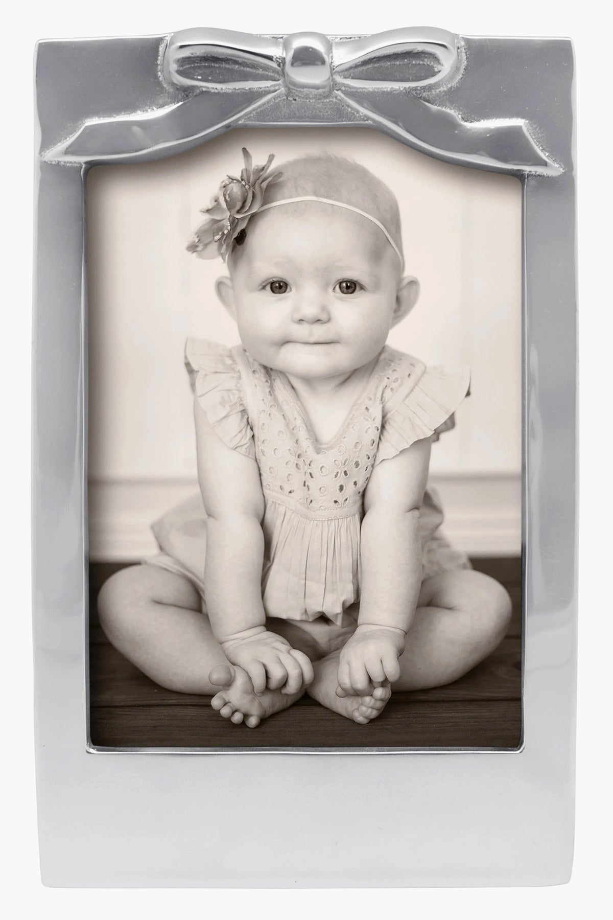 Black-and-white photo of a baby in a Mariposa 5x7 recycled aluminum frame with bow detail and flower headband—ideal as a baby shower gift.