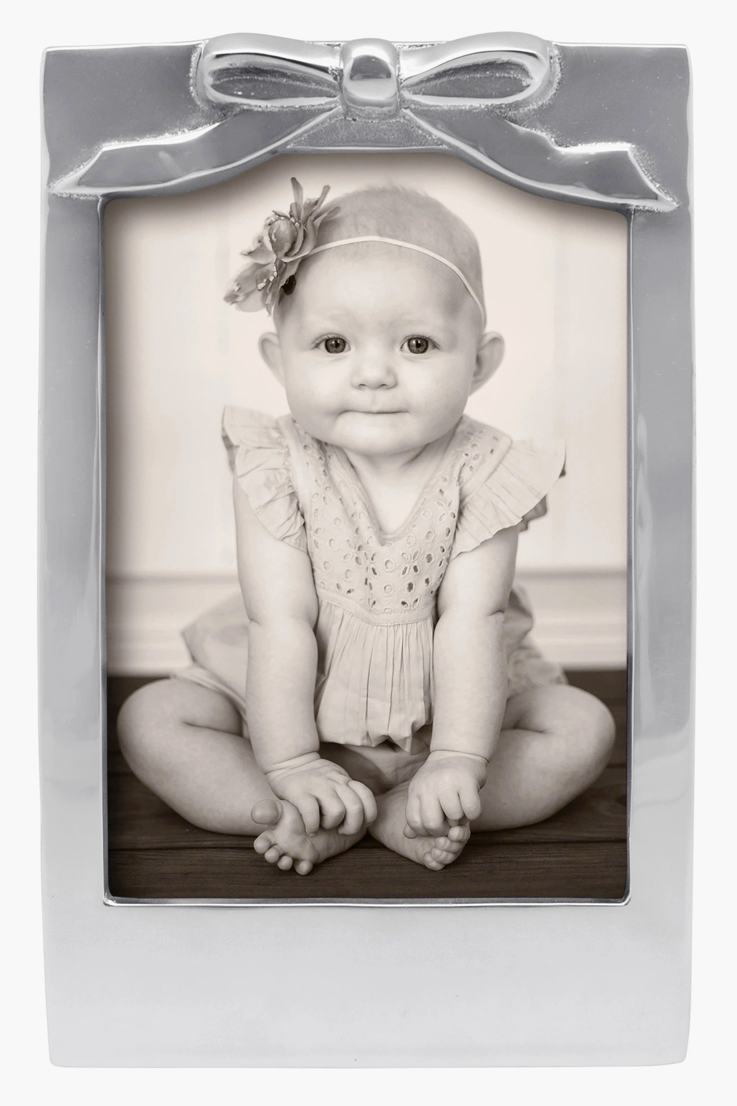 Black-and-white photo of a baby in a Mariposa 5x7 recycled aluminum frame with bow detail and flower headband—ideal as a baby shower gift.
