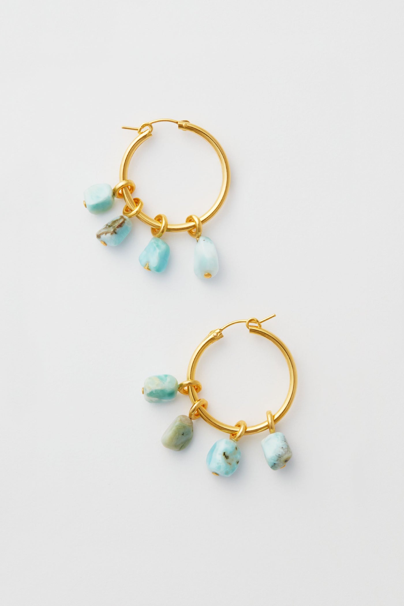 Lizzie Fortunato’s gold hoop earrings, each adorned with three dangling turquoise stone charms, beautifully highlight the art of handcrafted jewelry.