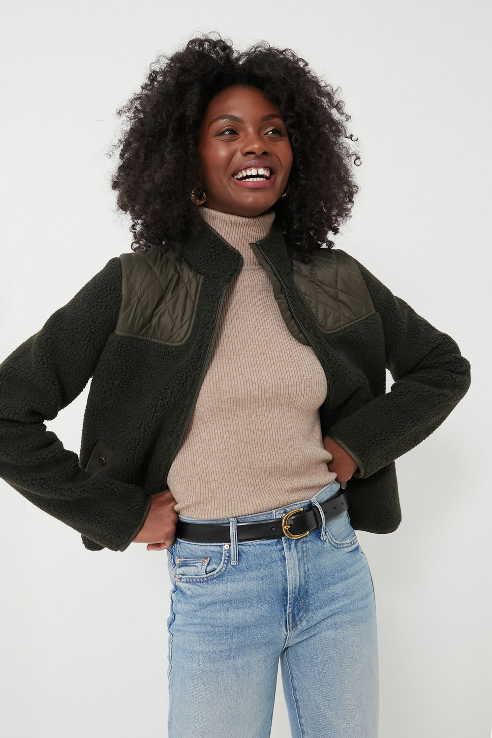 A woman smiling with hands on her hips, wearing a cozy Barbour sherpa jacket.