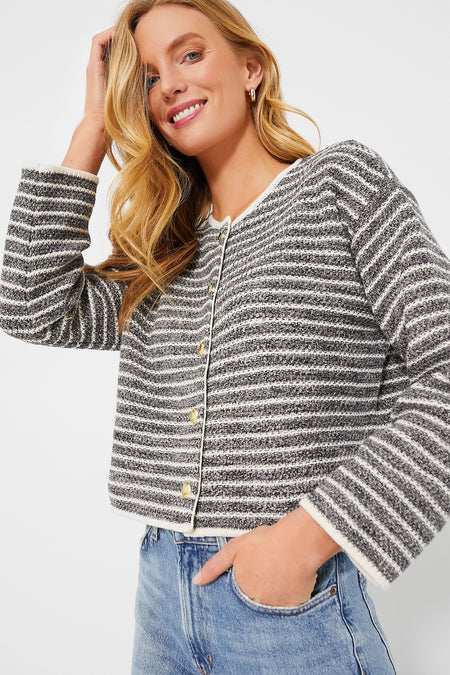 Woman wearing a Barbour black and white striped knitted cardigan with blue jeans, smiling and touching her hair.