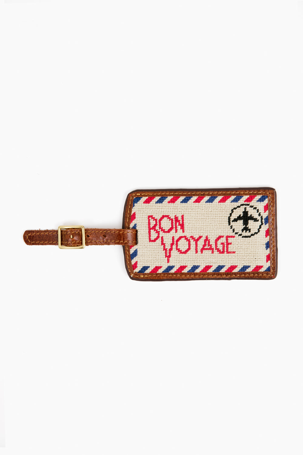 A Smathers and Branson rectangular needlepoint luggage tag with a brown strap, featuring hand-stitched "BON VOYAGE," an airplane, and a red-blue border inspired by an airmail envelope.