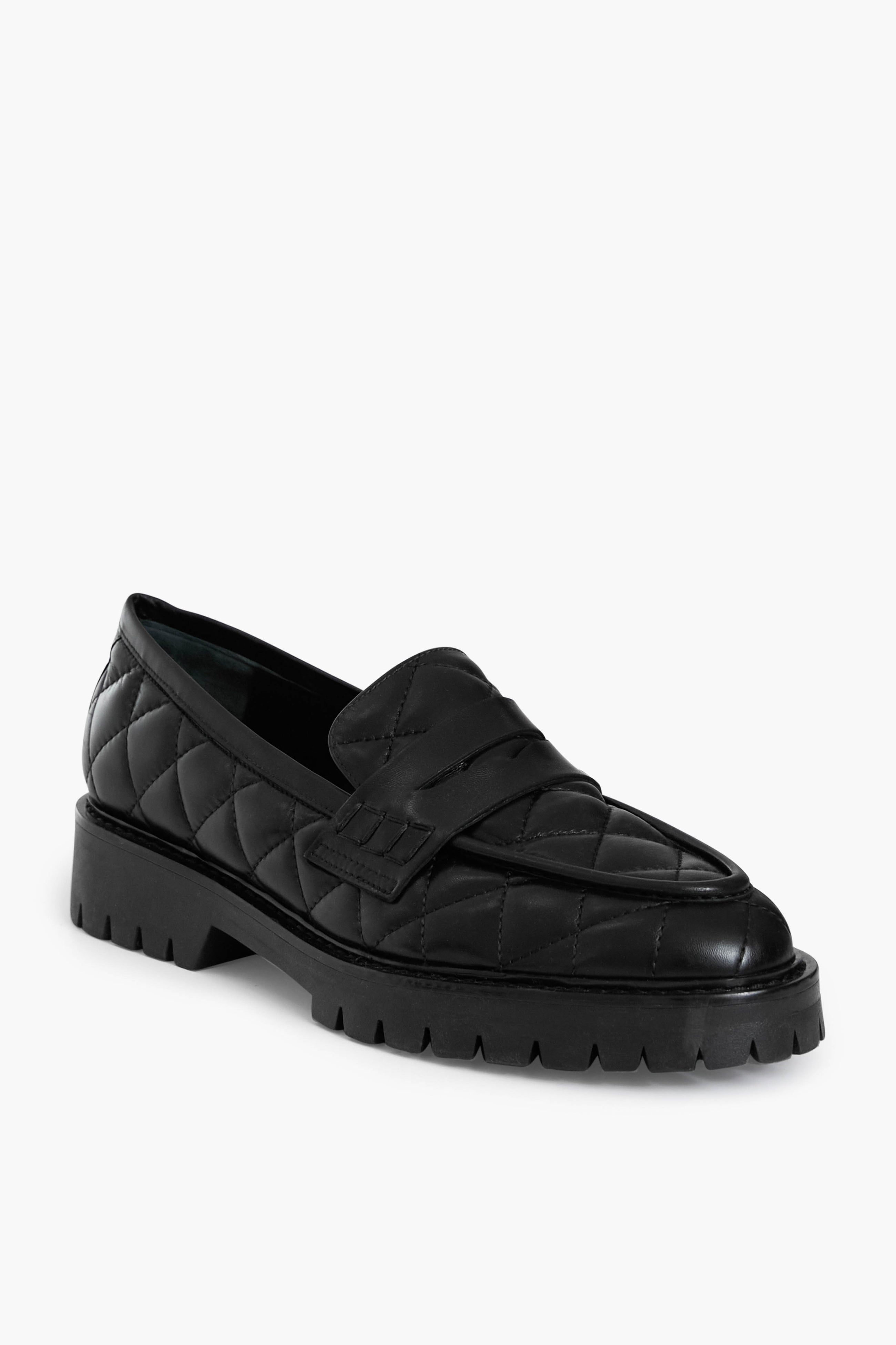 Flattered’s Black Signe Loafers in quilted leather feature a chunky sole and a decorative strap, blending handmade elegance with contemporary style.