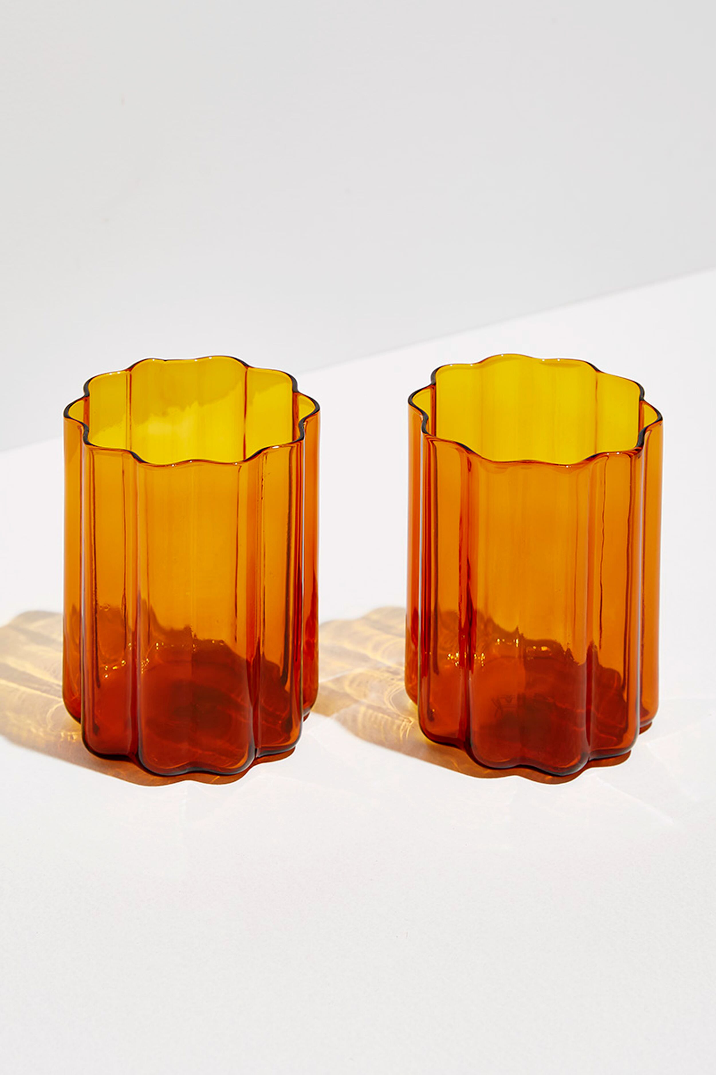 Two FAZEEK scalloped tumblers, crafted from hand-blown borosilicate glass, sit side by side on a white surface and cast faint shadows.