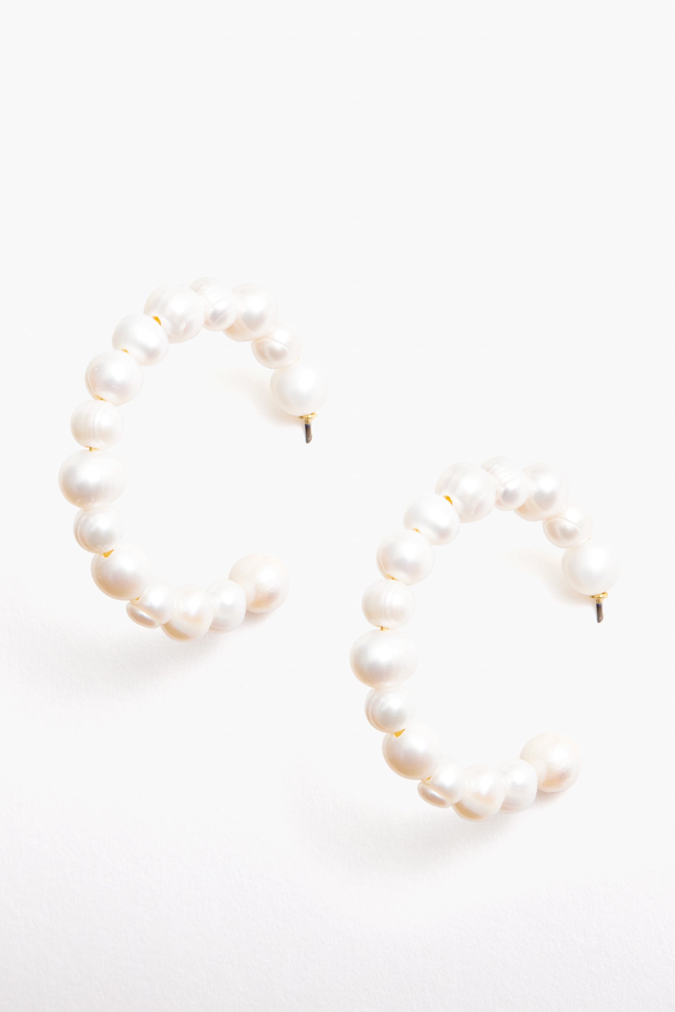 Tuckernuck Jewelry’s pearl hoop earrings feature round freshwater pearls in a semi-circle design. These hypoallergenic earrings provide timeless elegance and comfort for every occasion.