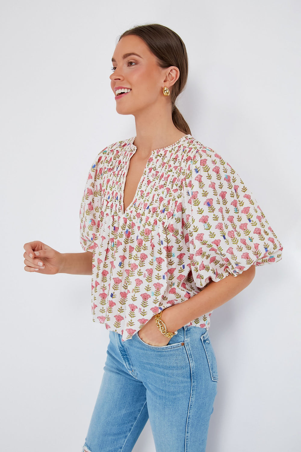 A woman wears the Saylor Cherry Blossom Jiby Blouse with puff sleeves, light blue jeans, and gold jewelry for a stylish, feminine look.