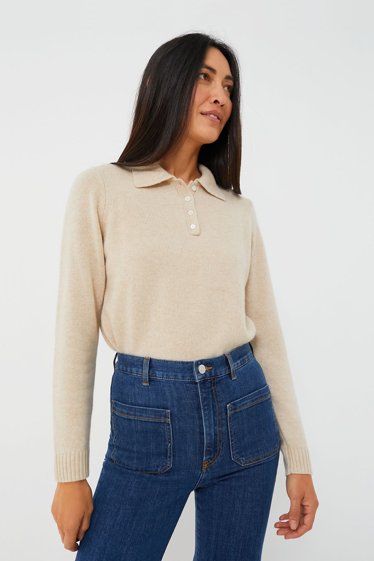 A woman wears a beige long-sleeve collared button-up sweater from Alex Mill and high-waisted blue jeans.