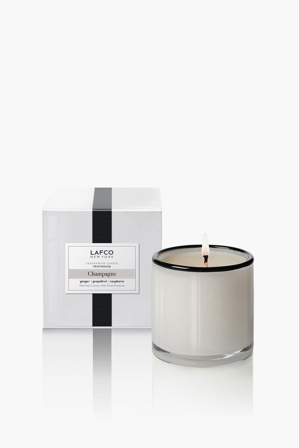 A white candle in a clear glass jar is lit beside its LAFCO New York Champagne Signature Candle box—a luxurious home fragrance and perfect housewarming gift.