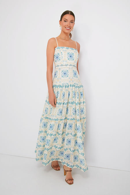 A woman smiles brightly wearing a sleeveless, ankle-length tropical floral dress in blue and yellow patterns by AGUA BY AGUA BENDITA.