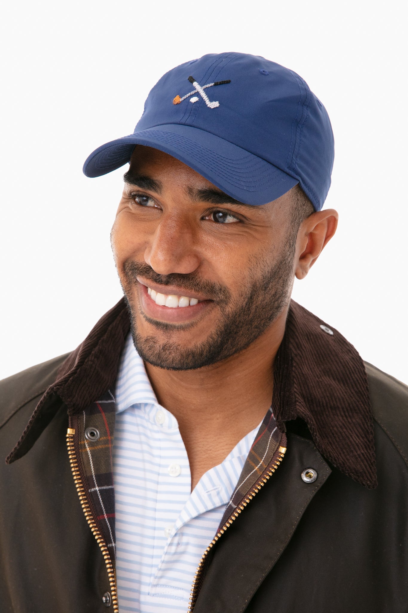 Smiling man in a Smathers and Branson blue needlepoint hat with crossed golf clubs, a striped collared shirt, and a dark jacket with corduroy collar—perfect style for any golf lover.