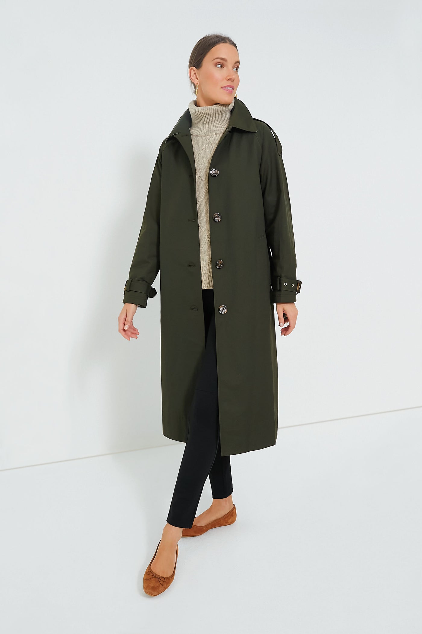 A woman stands confidently in a dark green Barbour Marie Showerproof Jacket, beige turtleneck sweater, black pants, and brown flats.