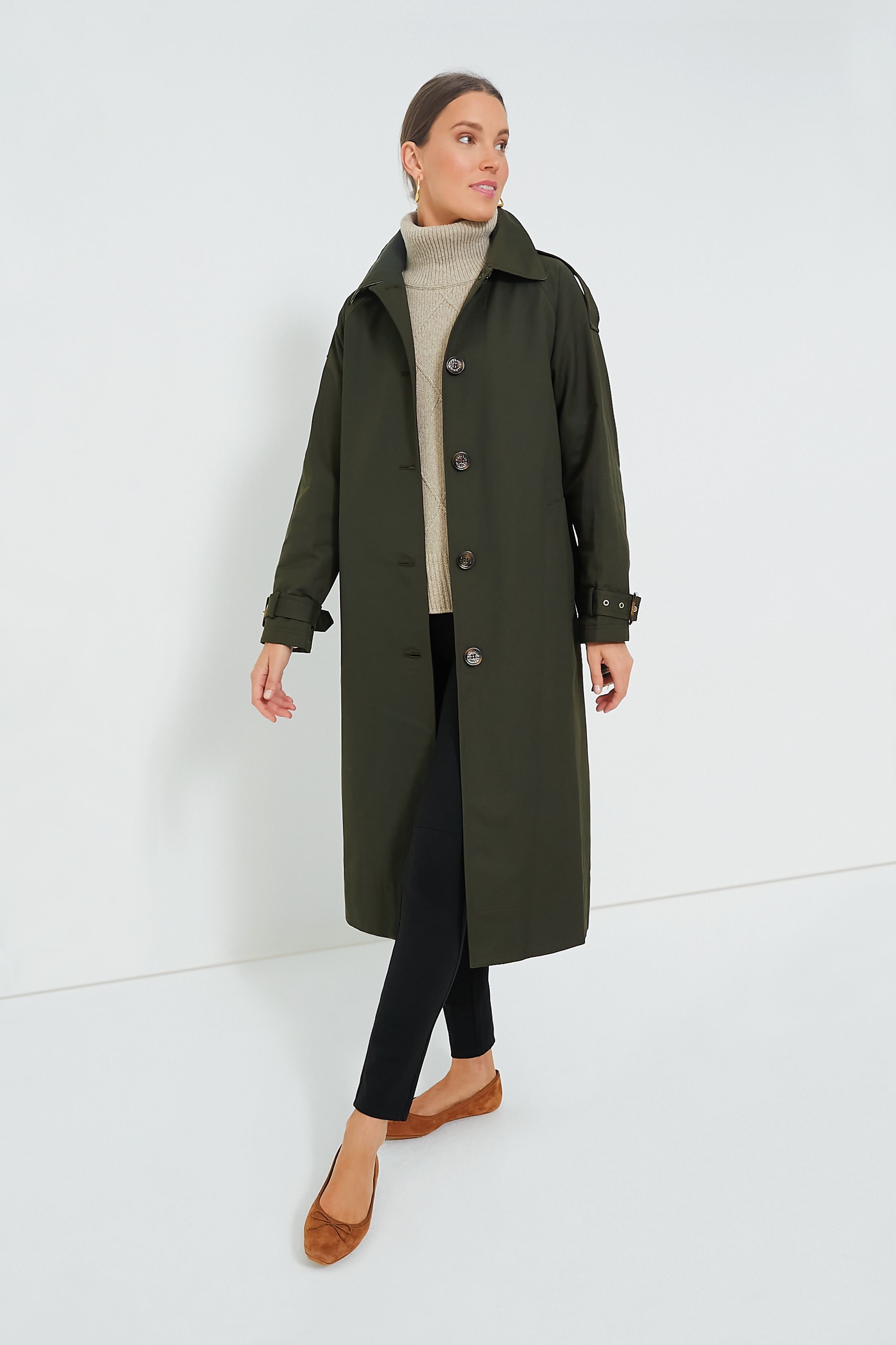 A woman stands confidently in a dark green Barbour Marie Showerproof Jacket, beige turtleneck sweater, black pants, and brown flats.