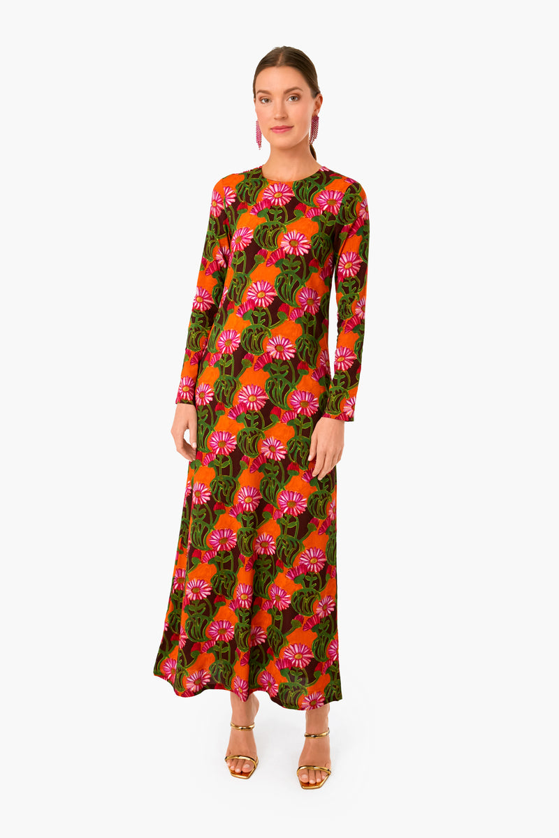 A woman wears a La DoubleJ long-sleeved, ankle-length maxi dress with a pink and green floral print, paired with gold sandals and pink earrings.