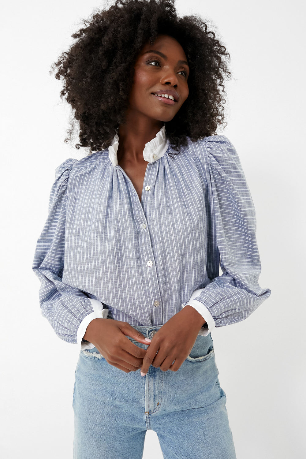 A person wears an Alix of Bohemia Blue Chambray Annabel Shirt with puffed sleeves and a ruffle collar, paired with light blue jeans.