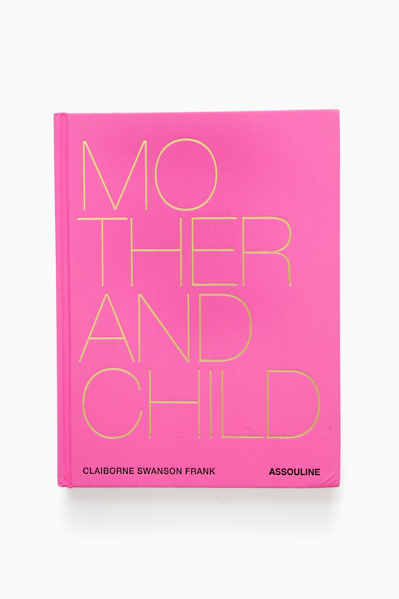 A pink hardcover book titled "Mother and Child" by Claiborne Swanson Frank, published by Assouline, showcases bold yellow cover text and vibrant portraits that celebrate modern motherhood.