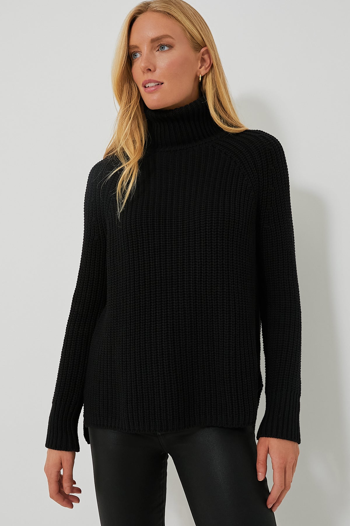 A woman wears a black 525 America Shaker Turtleneck sweater with black leather pants, creating a chic, streamlined look.