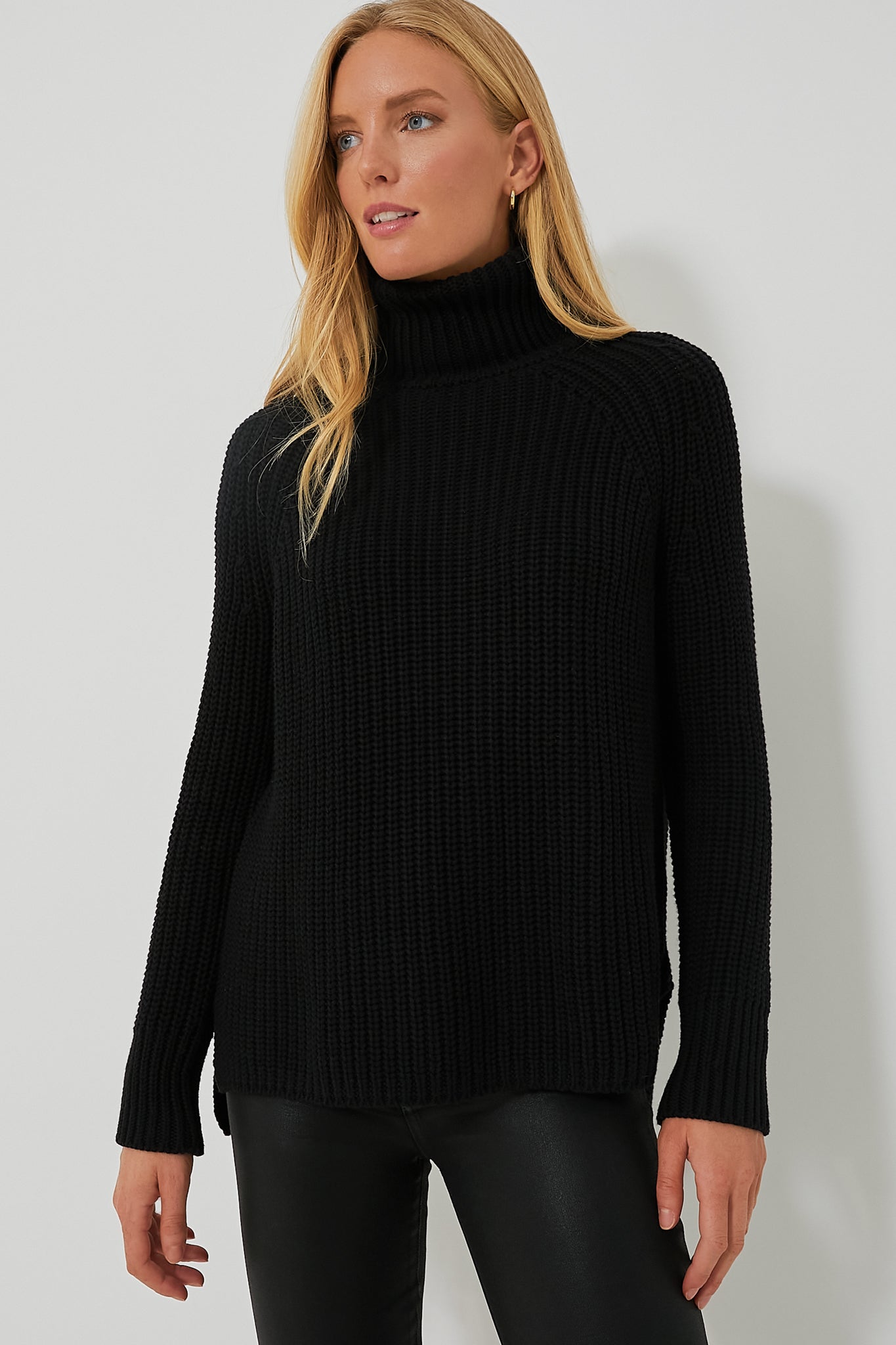 A woman wears a black 525 America Shaker Turtleneck sweater with black leather pants, creating a chic, streamlined look.