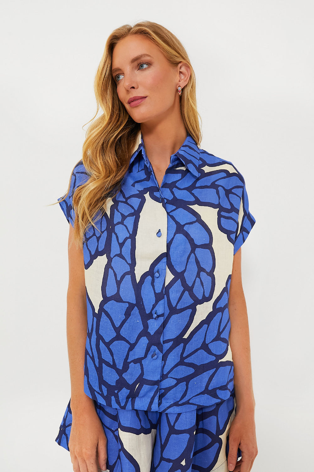 A woman with long blonde hair wears a Eugenia Fernandez linen button-down shirt and matching shorts featuring a bold blue and white abstract leaf pattern.