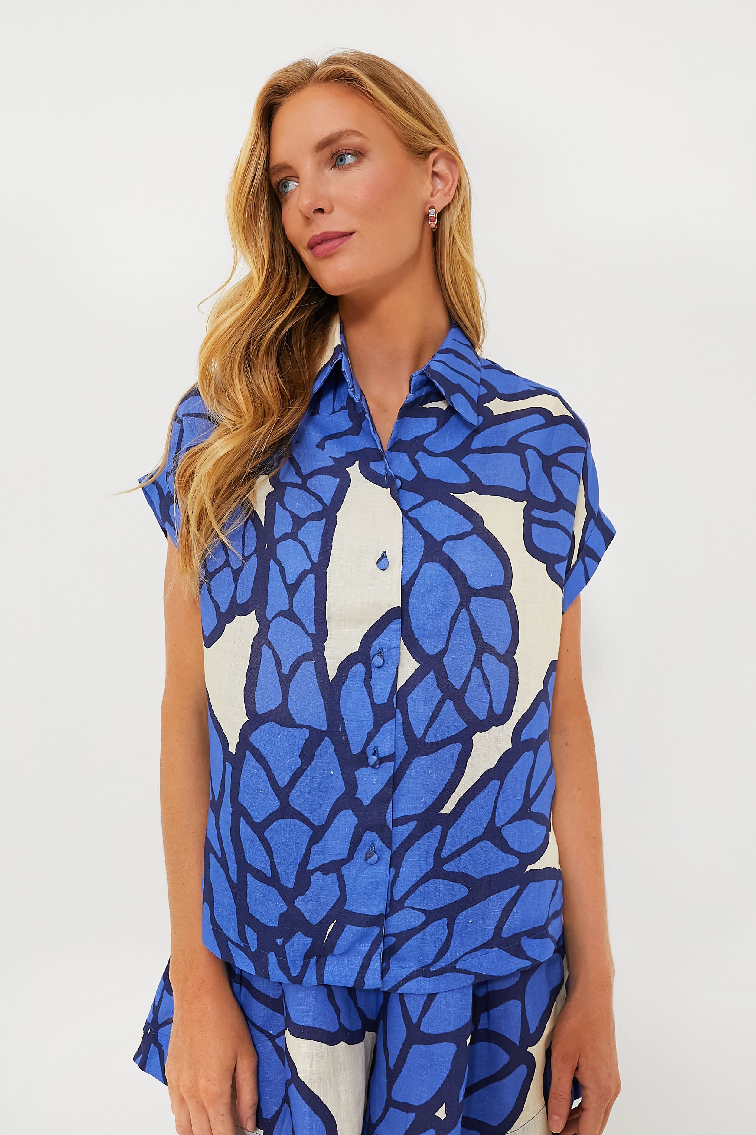A woman with long blonde hair wears a Eugenia Fernandez linen button-down shirt and matching shorts featuring a bold blue and white abstract leaf pattern.