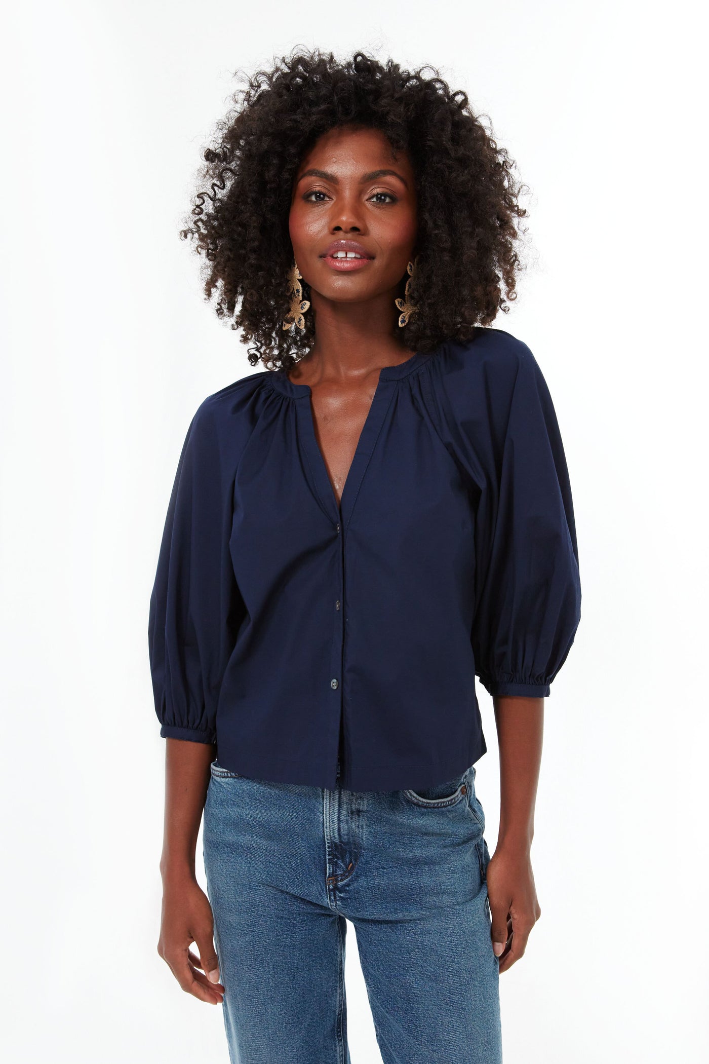 A woman with curly hair wears the STAUD Navy New Dill Top, a cotton poplin blouse with 3/4 puff sleeves, paired with blue jeans.