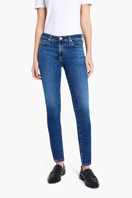 A person stands confidently in a white short-sleeve t-shirt, AG Jeans blue vintage Japanese denim jeans, and black loafers.