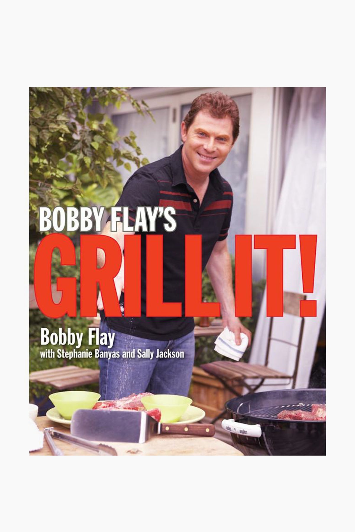 A man smiles at the camera while grilling steaks outdoors. The cover text reads: “Bobby Flay’s Grill It!”—a Rizzoli cookbook with grilled recipes, marinades, and co-authors listed below.
