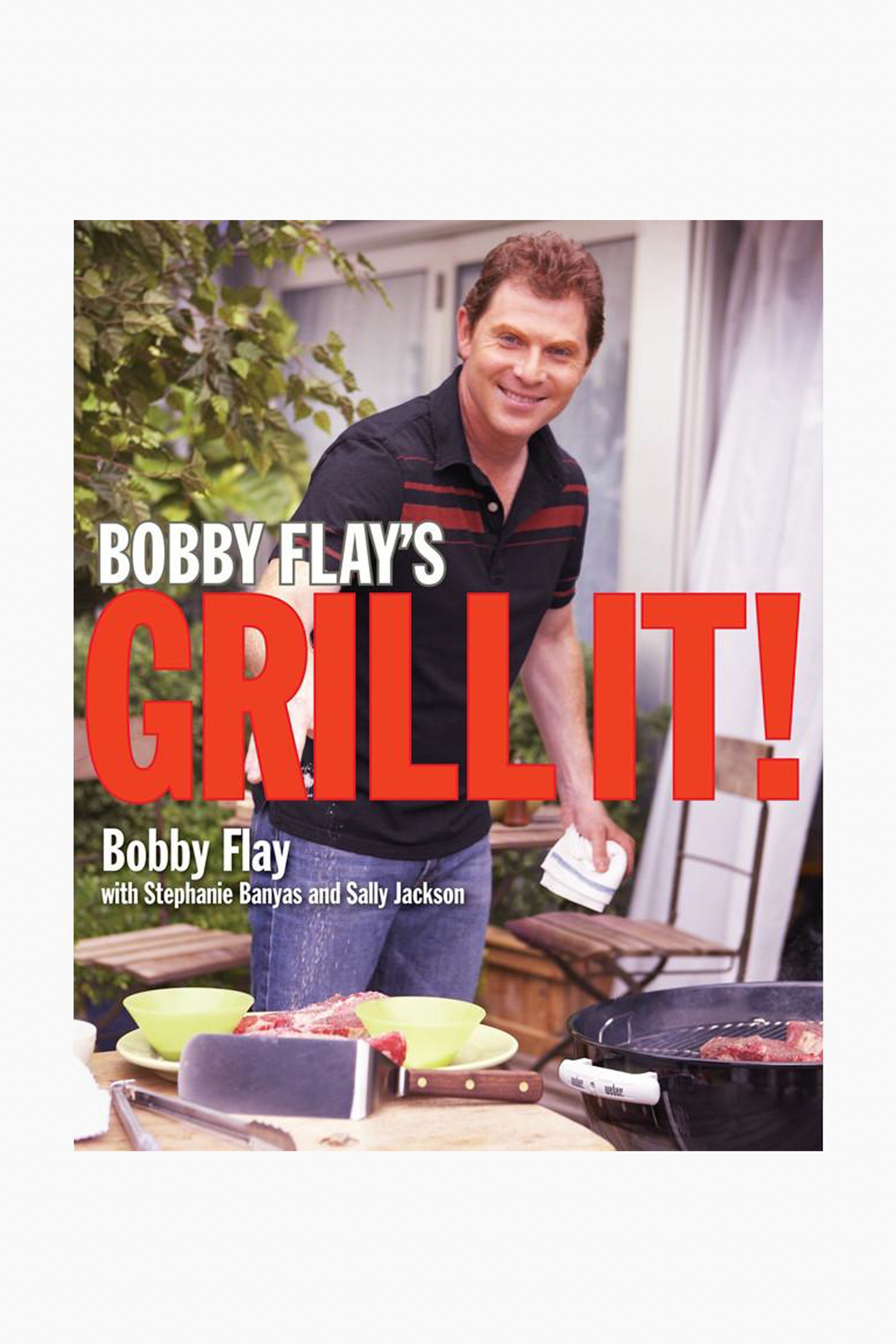 A man smiles at the camera while grilling steaks outdoors. The cover text reads: “Bobby Flay’s Grill It!”—a Rizzoli cookbook with grilled recipes, marinades, and co-authors listed below.