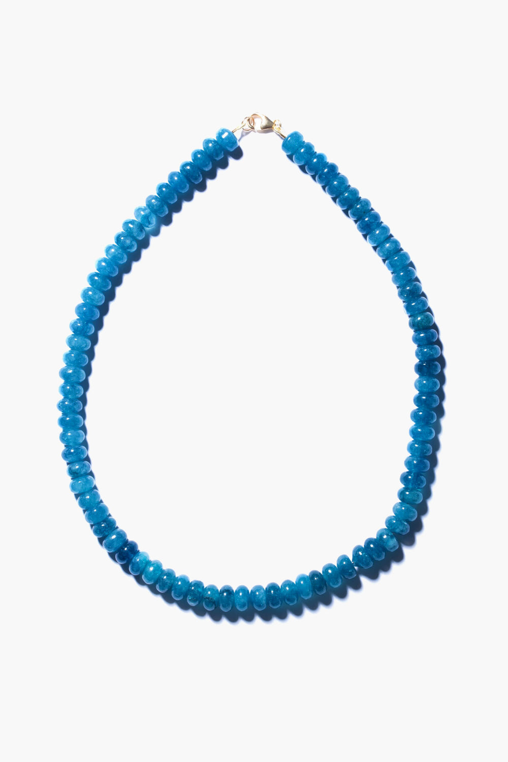 This handmade angelite necklace by Theodosia features round, bright blue beads with a small gold clasp, elegantly arranged in an oval shape—a stunning piece of jewelry.