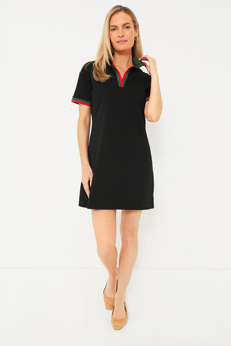 A woman wears a Tuckernuck black mini cotton A-line dress with short sleeves and red and green trim, paired with light brown flats.