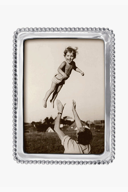 A black and white photo in a silver Mariposa 5x7 frame with beaded trim shows an adult tossing a smiling child outdoors, with tents nearby.