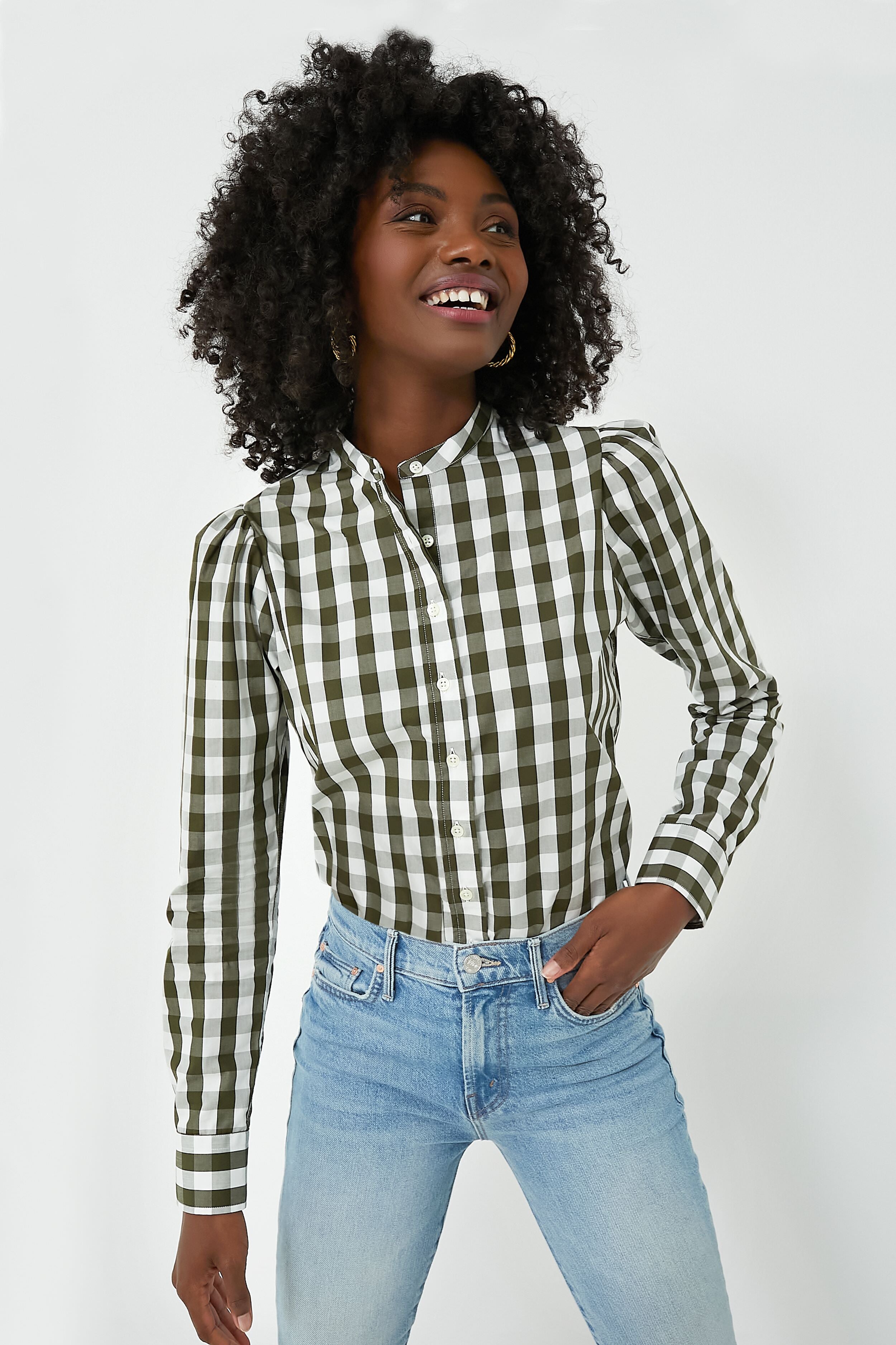 Wearing The Shirt by Rochelle Behrens, a person in a green and white checkered cotton shirt and light blue jeans stands, smiling and looking to the side.