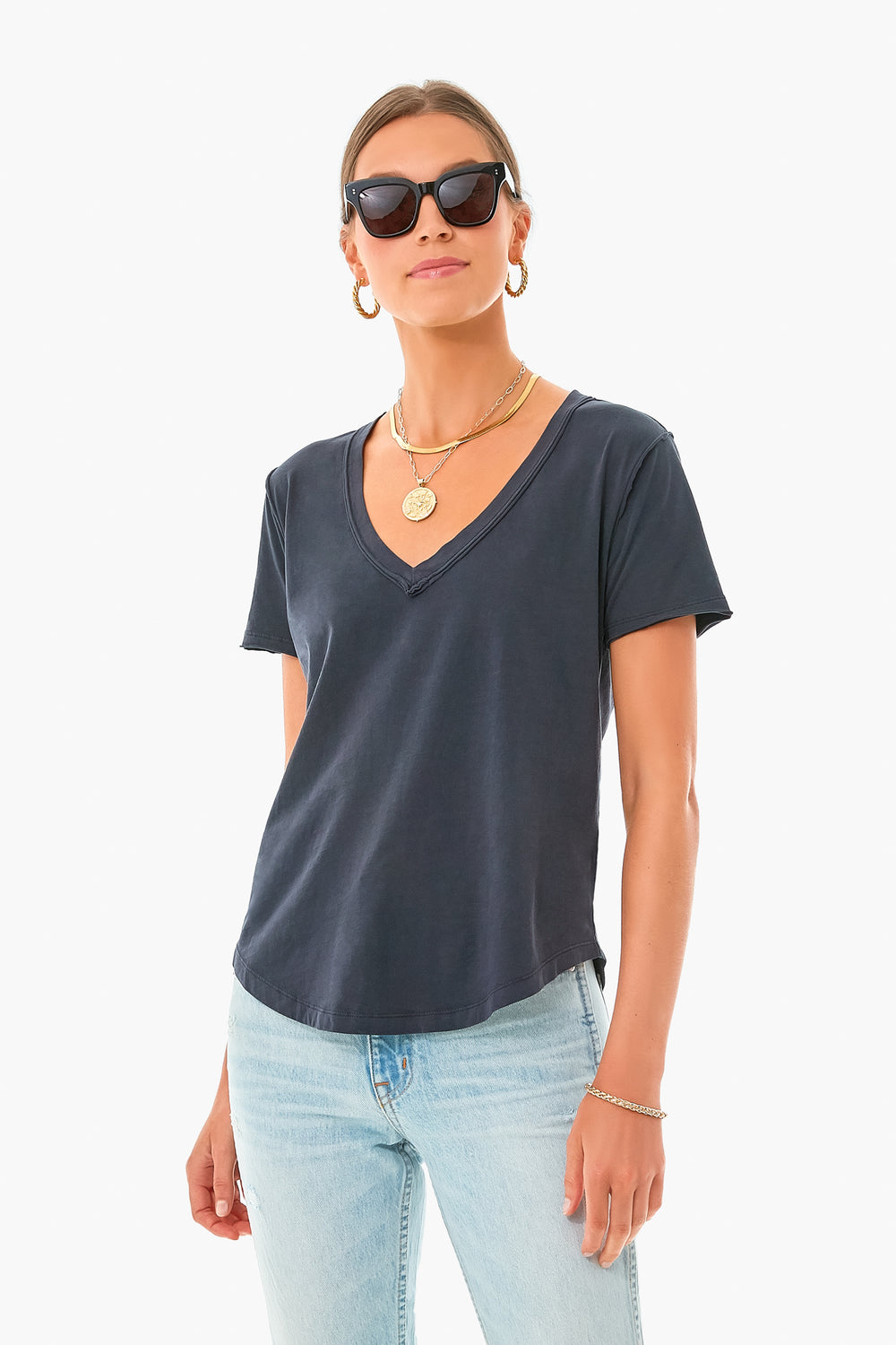 A person stands confidently wearing sunglasses, gold jewelry, a Z SUPPLY Black V Neck Tee made from organic cotton, and light blue jeans.