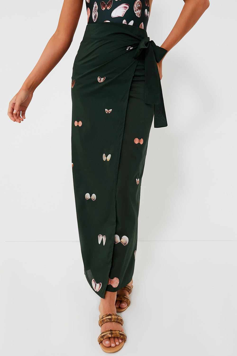 Wearing an AGUA BY AGUA BENDITA black wrap skirt with seashell motifs, a sleeveless top, and brown sandals creates a breezy, effortless look.