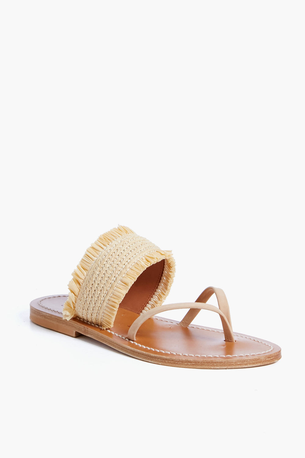 The K.Jacques sandal features a flat tan leather sole, a thin toe strap, and a wide woven raffia strap with fringe detailing across the top.