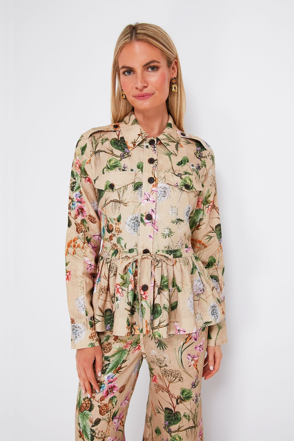 A woman wears a Cara Cara beige floral print linen peplum jacket with waist tie and matching pants, styled for a chic look.