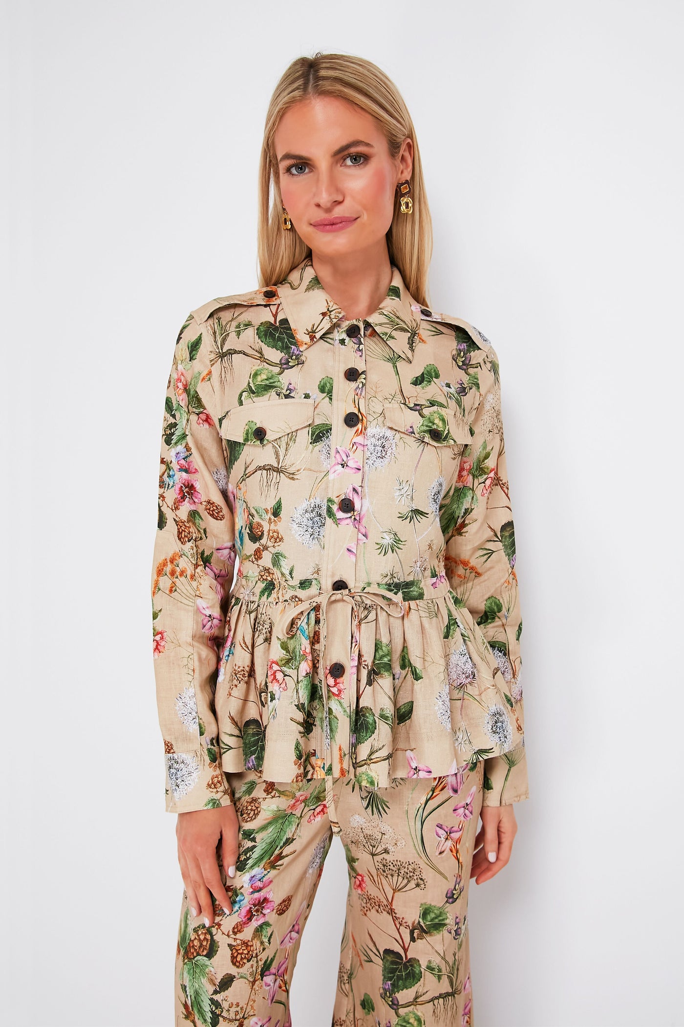 A woman wears a Cara Cara beige floral print linen peplum jacket with waist tie and matching pants, styled for a chic look.