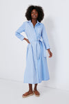 A woman wears a Tuckernuck light blue and white striped maxi shirt dress with long sleeves and a waist tie, paired with tan slip-on sandals.