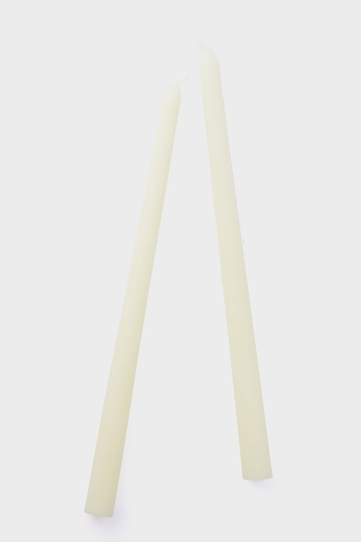 Two unlit, off-white Greentree Home handmade candles stand upright and lean together so their tips touch, showcasing the elegant simplicity of these cream tapers.