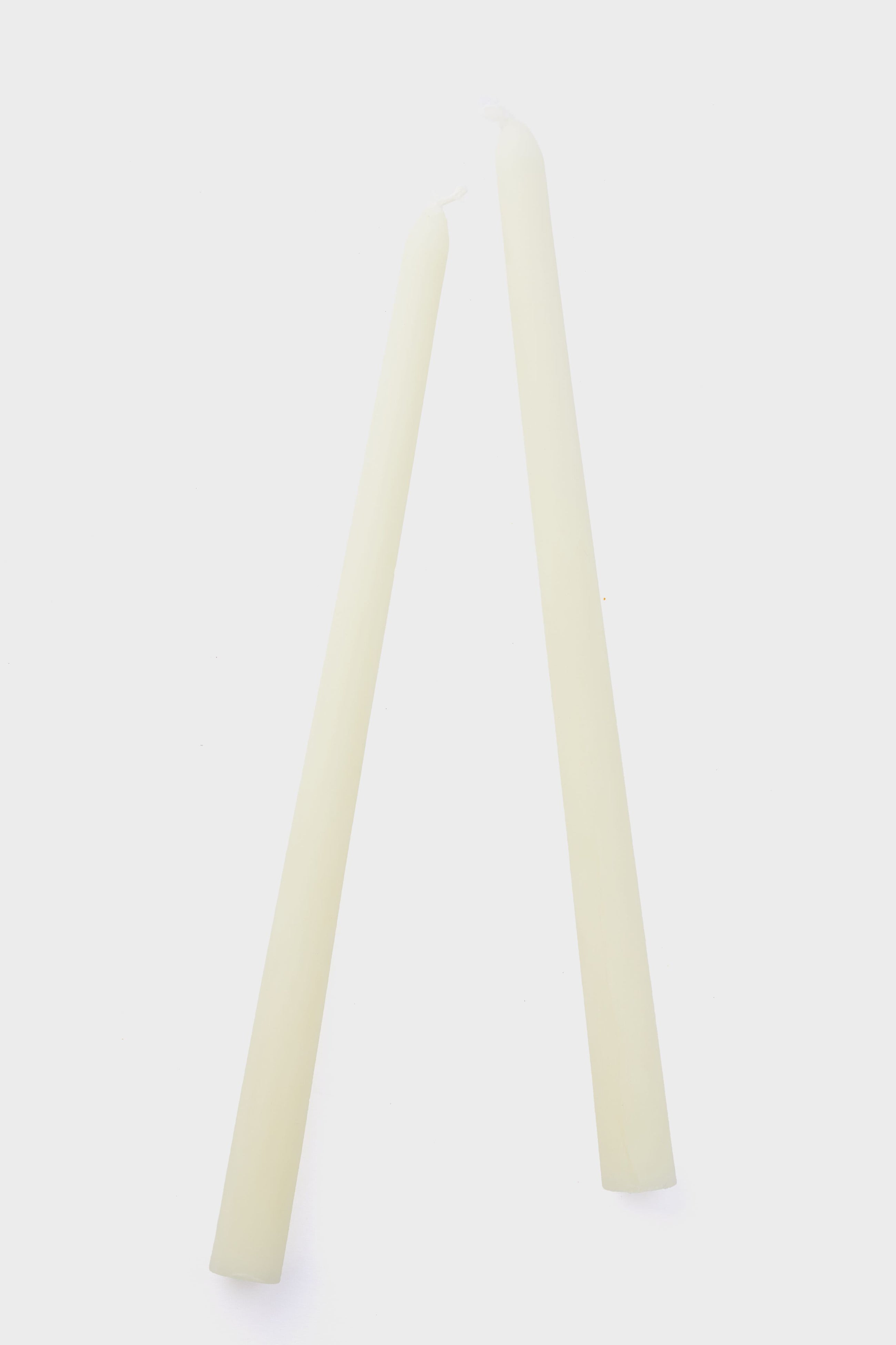 Two unlit, off-white Greentree Home handmade candles stand upright and lean together so their tips touch, showcasing the elegant simplicity of these cream tapers.